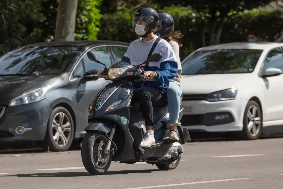Pareja en moto, &iquest;con cu&aacute;ntos a&ntilde;os puedes conducir una moto de 49? Ambos llevan casco y mascarilla.