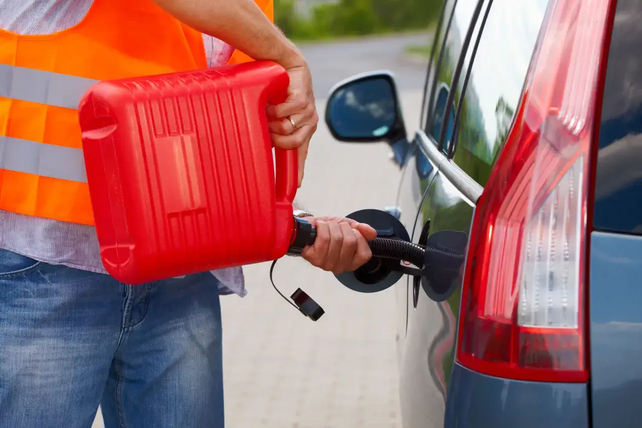 Hombre con chaleco naranja vierte gasolina de un bid&oacute;n rojo a un coche sin gasolina.