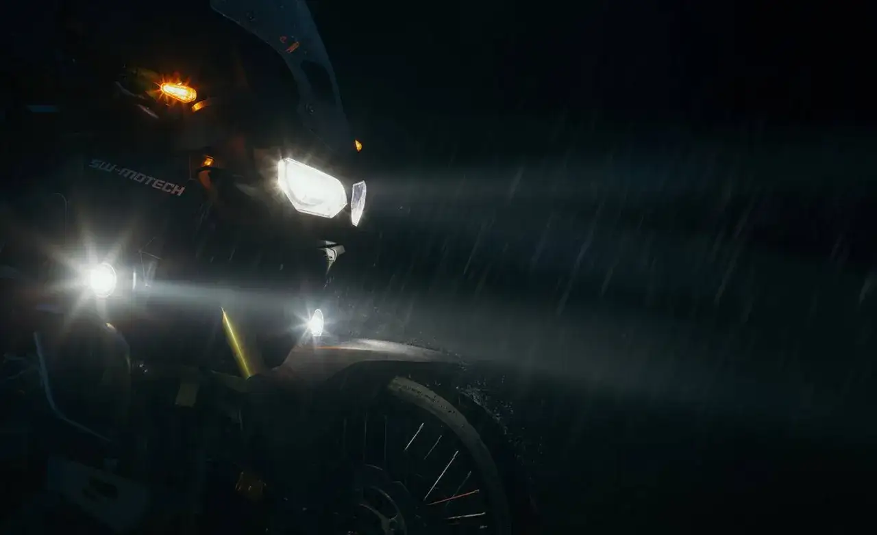 Motocicleta con potentes luces, incluyendo luz antiniebla, iluminando la noche lluviosa.