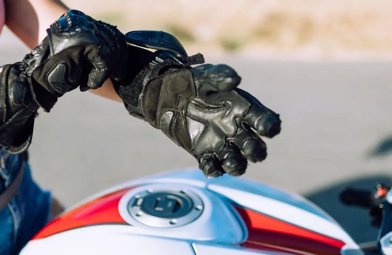 Persona se prepara para conducir su moto, ajustándose unos guantes de cuero. Es obligatorio llevar guantes en moto para protegerse.