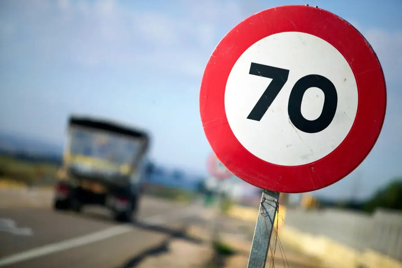 Señal de velocidad mínima de 70 en carretera convencional. Un camión borroso avanza por la vía.