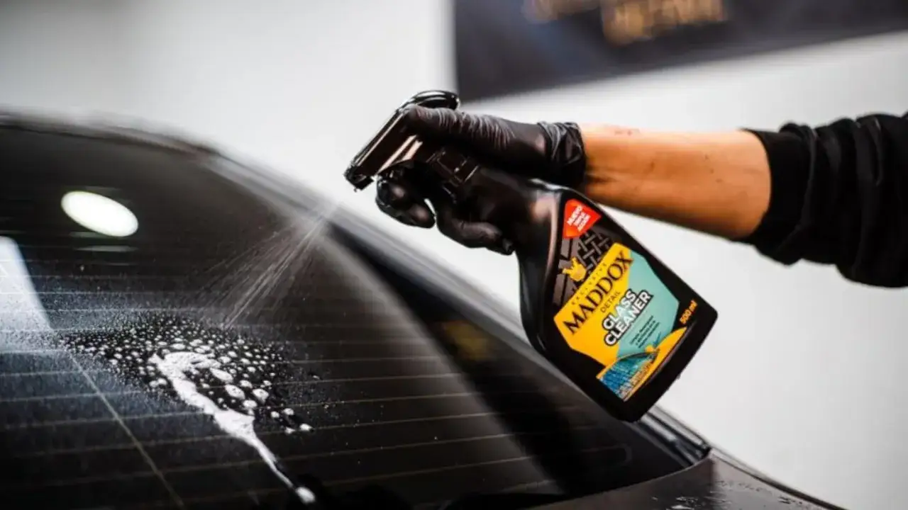 Mano con guante negro roc&iacute;a limpiador Maddox en el cristal trasero de un coche. Aprende como limpiar los cristales del coche para que queden perfectos.