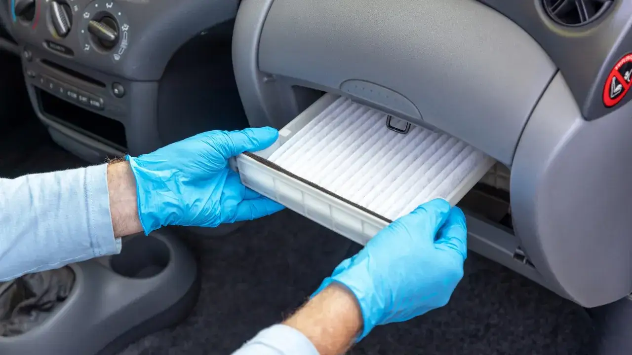 Man con guantes azules saca un filtro de aire acondicionado de coche.