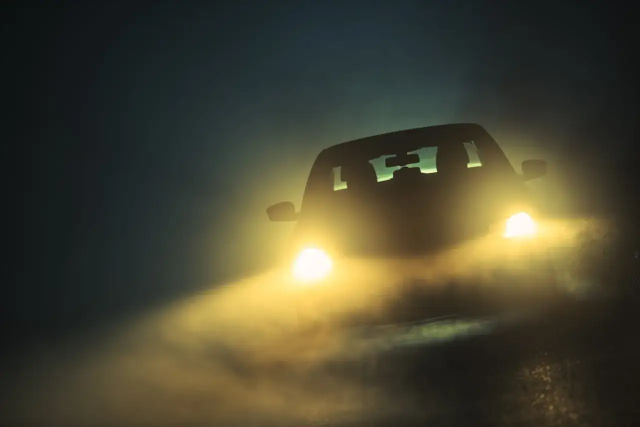 Un coche avanza en la densa niebla, sus luces antiniebla obligatorias iluminan el camino.
