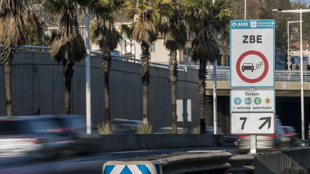 Se&ntilde;al de ZBE en Barcelona. Prohibido circular sin la etiqueta c o veh&iacute;culos autorizados. Palmeras y coches en movimiento.