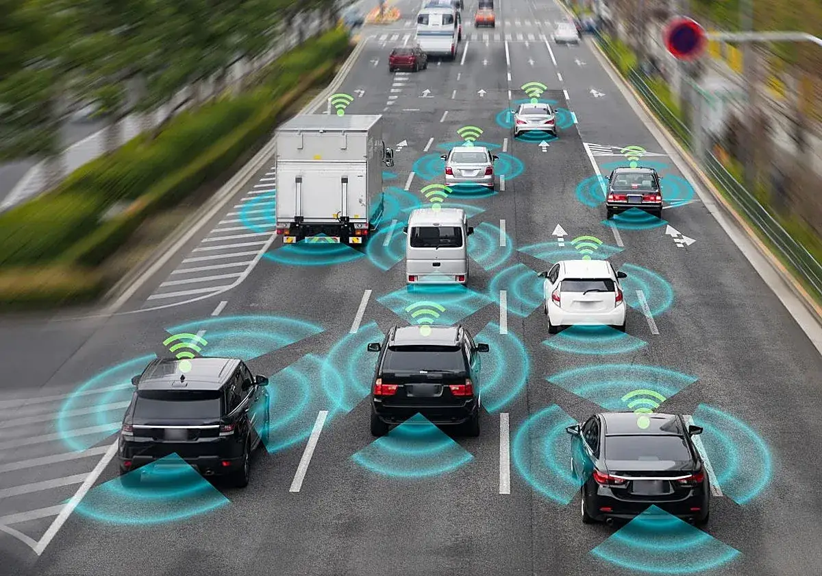 Varios coches y un cami&oacute;n circulan por una autopista, cada uno con un icono de Wi-Fi verde y ondas azules que indican la comunicaci&oacute;n de un coche aut&oacute;nomo.