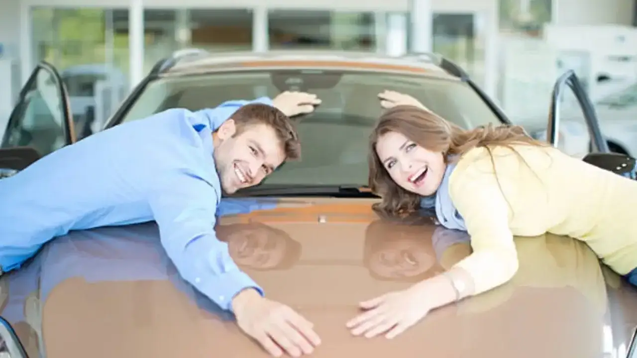 Pareja feliz abrazando el capó de un coche nuevo, planeando cómo poner coche a nombre de dos personas.