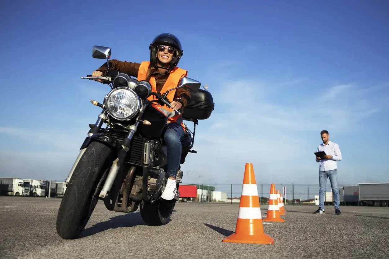 Mujer sonriente en moto, lista para sacar carnet a2 teniendo el b. Instructor observa en fondo.