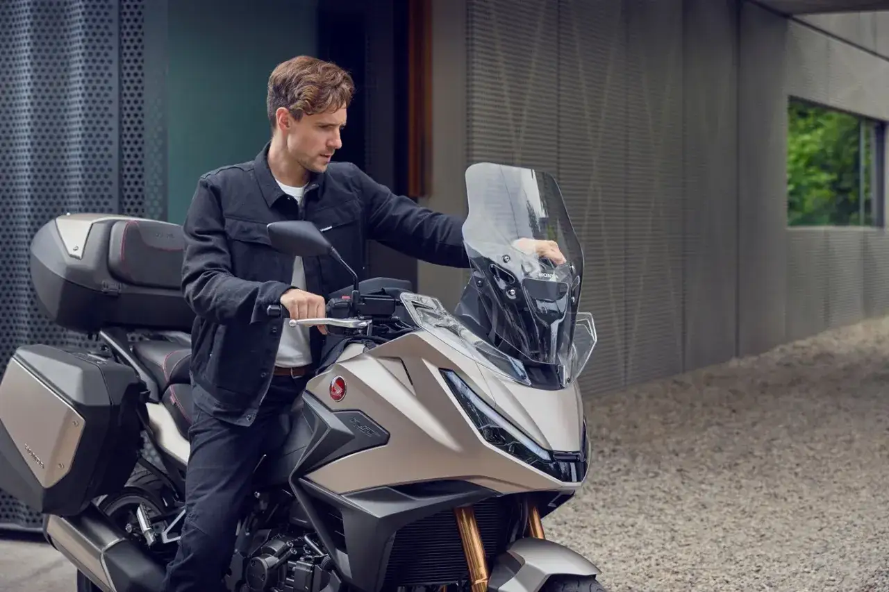 Hombre con chaqueta negra ajustando la pantalla de una moto Honda con maletas. Ideal para la nueva normativa motos 125.