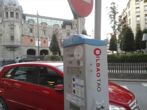 Máquina de parquímetro con el logo de BILBAO TAO en una calle de Bilbao. Un coche rojo está aparcado al lado.