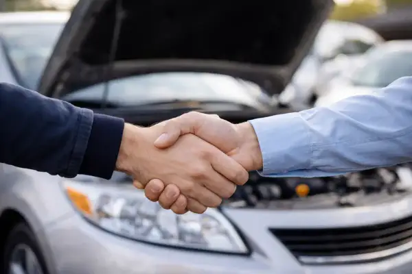 Dos hombres se dan la mano frente a un coche con el capó abierto. Un acuerdo sellado, el tfsi significado de una transacción exitosa.