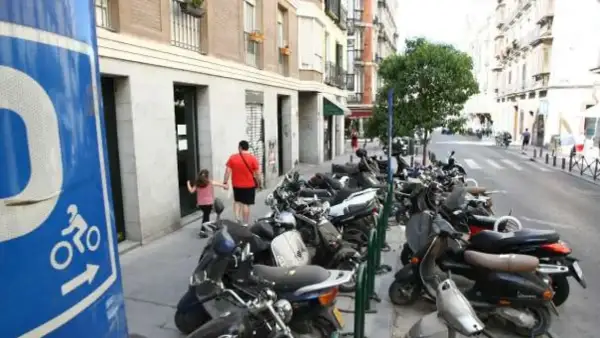 Señal azul de normativa aparcamiento motos. Calle con muchas motos aparcadas y un padre con su hija caminando.