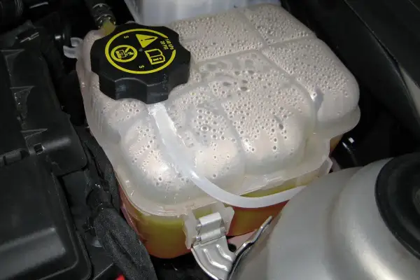 Depósito de expansión con líquido refrigerante y burbujas. Es hora de rellenar líquido refrigerante para mantener el motor fresco.