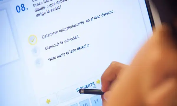 Persona realizando el test DGT A1 en una pantalla táctil. La pregunta 8, con una opción marcada, se centra en la señalización.