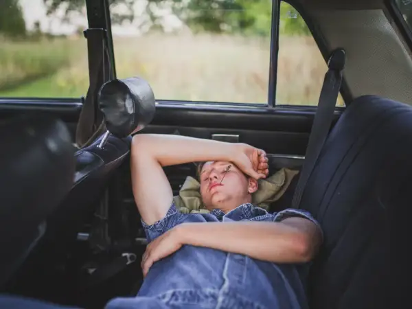 Joven duerme en el asiento trasero de un coche, con una brizna de hierba en la cara. Se puede dormir en el coche en un viaje largo.