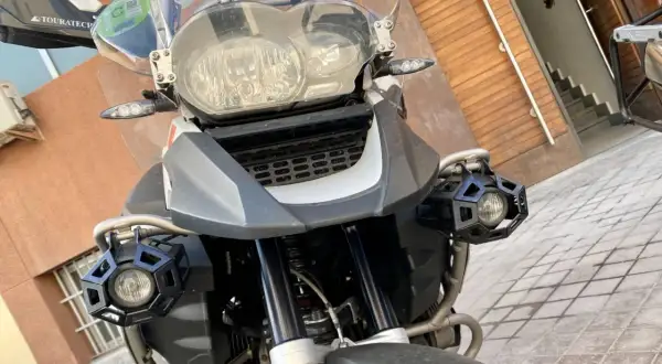 Detalle frontal de una motocicleta con dos luces antiniebla hexagonales negras montadas en los laterales.