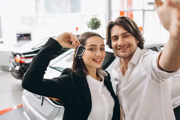 Pareja feliz celebrando la compra de un coche nuevo, ella muestra las llaves. ¡Ya pueden poner el coche a nombre de dos personas!