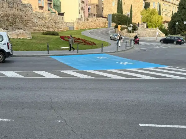 Paso de peatones azul en la zona bajas emisiones de Tarragona, con restos arqueológicos al fondo.
