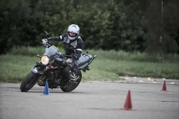 Motociclista en entrenamiento, practicando maniobras para obtener su **permiso a**. Conos marcan el circuito.