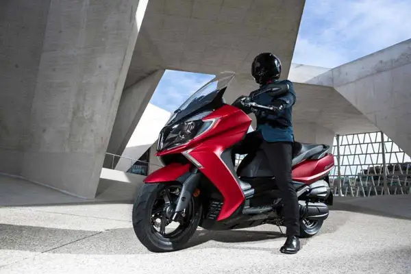 Hombre con casco negro posa junto a un ciclomotor rojo brillante, listo para la aventura urbana.