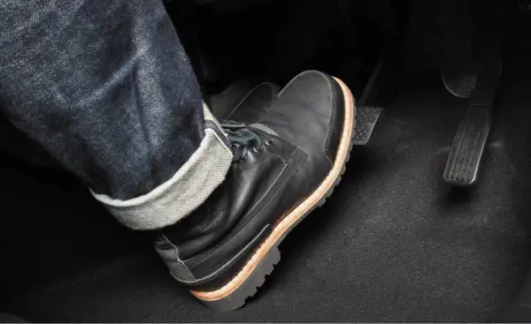 Pie con bota negra pisando el pedal del embrague. Para frenar hay que pisar el embrague y luego el freno.