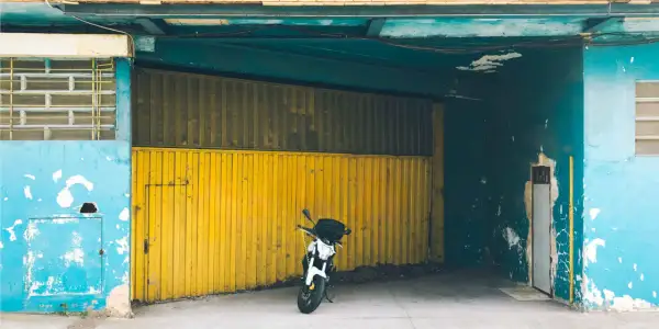 Una moto blanca espera en una cochera con puerta amarilla, donde se puede aparcar sin vado.