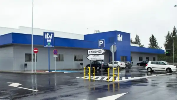 Edificio azul y gris de **itv extraordinaria** con señales de tráfico y coches aparcados en un día lluvioso.