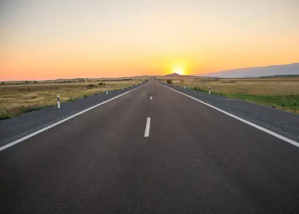 Una carretera convencional se extiende hacia el horizonte bajo un atardecer dorado.