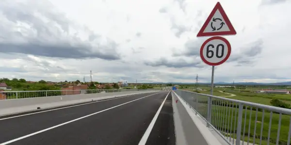 Señal de tráfico indica velocidad minima en carretera convencional de 60 km/h, con un cruce de rotonda cercano.