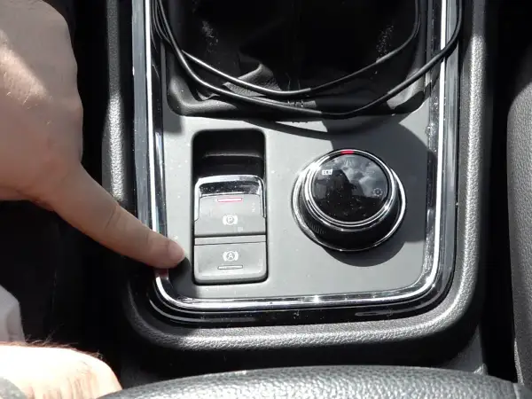 Dedo presionando el botón de freno de mano electrónico, que es parte del sistema auto hold.