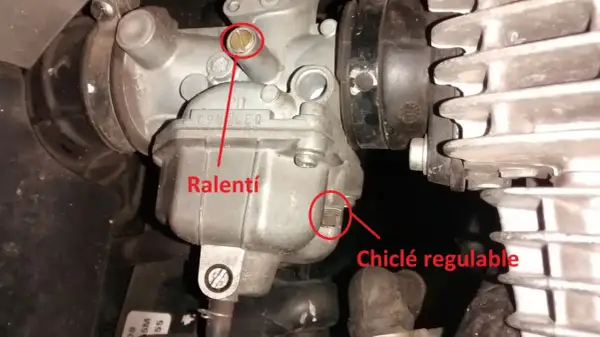 Detalle de carburador de moto, mostrando el tornillo de ralentí y el chiclé regulable.